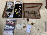 Overview of collection items including cufflinks, pocket knives, coins, lapel pins, watch bands, coin purse, and various trinkets within two valet boxes and tray.