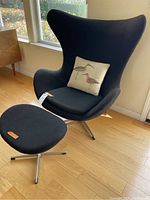 Side-angle view of black egg chair and matching ottoman near window