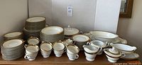 Full view of the Noritake China set including stacked plates, cups, bowls, and serving pieces on a wooden surface against a whiteboard.