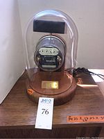 Full view of the Westinghouse vintage energy meter under clear glass dome on wooden base with auction label and pricing notes on surface.