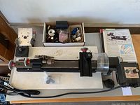 Entire lathe mounted on board with headstock, carriage, tailstock, power cord, manual and accessory boxes visible