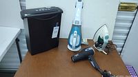 Full view showing the four appliances: shredder, handheld vacuum, steam iron, and hair dryer arranged on white surface.