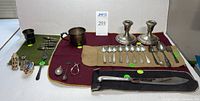 Overview of lot on burgundy mat showing candlesticks, flatware, cups, knife, forks, lipstick holders, and corn holders