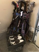 Two golf bags filled with clubs, including MacGregor and Callaway brands, with club covers. FootJoy Gel Fusion golf shoes size 9W in a box are placed on a bucket.