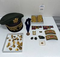 Overview of entire lot showing hat, epaulets, medal, badge pieces, ribbon bars, buttons, and rank patches.