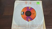 Top view of a 45rpm vinyl record by Sonny & Cher titled 'I Got You Babe' with Kapp label in orange and purple, housed in a Warner Bros. Records paper sleeve.