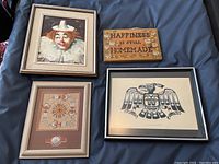 Full view of four items displayed on fabric backdrop: clown painting, wooden sign, indigenous sand art, Haida Thunderbird print