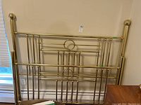 Full view of the brass metal headboard showing vertical and horizontal bars with circular decorative elements and finials on posts.