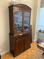 Full view of the antique wooden china cabinet showing top glass doors, carved pediment, drawer and bottom cabinet doors.