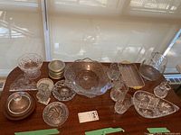 Overview of all crystal and glass items on table including bowls, trays, glasses, napkin holder, and ashtrays.