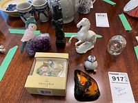 Overview photo of the figurines lot showing the stone parrot on geode, Asian figurine, porcelain horse, ceramic puffin, ceramic bird, glass bear, and painted glass stone.