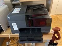 Front and angled view of the black HP Officejet Pro 8610 printer showing paper input and output trays, control panel and ink cartridge label.
