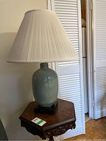 Full view of the lamp showing the ceramic base and pleated fabric shade on a wooden table.