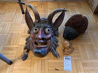 Photo showing all three items together placed on a hardwood floor: hand carved wooden mask with two large horns (one damaged), wooden cherub bust, and a hedgehog shaped boot brush with composite head and straw bristles.