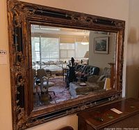Front view of large rectangular wall mirror with ornate carved wood frame and beveled glass reflecting room interior