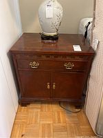 Front view of the Baker Furniture nightstand showing drawer, cabinet doors and overall dark wood finish with carved accents