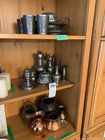 Shelves showing an assortment of pewter, copper, brass items and an iron cauldron.