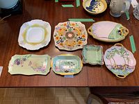 Eight assorted porcelain plates displayed on a wooden table with various floral and decorative designs.