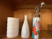 Photo showing two white Rosenthal vases and one colorful floral Royal Doulton vase on a wooden shelf.