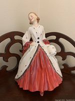 Front view of Royal Doulton figurine The Ermine Coat in white with red skirt, showing detailed hand-painting and posed stance.
