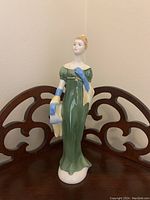 Front view of Royal Doulton Lorna figurine in green dress with blue glove and yellow shawl.