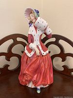 Front view of Royal Doulton Christmas Morn figurine showing the detailed red dress, white fur-trimmed coat, green bonnet and white muff near face.