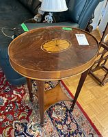 Front angled view of the oval top with inlay design and upper finish flaws visible, side legs, and lower shelf.