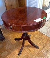 Round wood side table with claw feet legs and two drawers with metal pulls, pictured from top angle showing circular tabletop and metal pull on drawer with finish flaws.