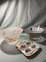 Two large bowls shown on white backdrop, one frosted with floral pink rose design and the other clear with black and white houndstooth pattern, plus a package of holiday cookie cutters