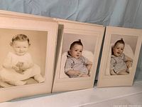 Three baby photos in original folders: one black and white boy with toy, two colorized girl reclining in blue outfit.