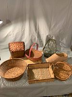 Photo showing 8 assorted baskets, including vintage green basket and new style shoe basket, arranged on white backdrop.