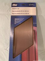 Photo showing factory sealed bronze kickplate in original packaging with National Gallery branding and measurements on top.