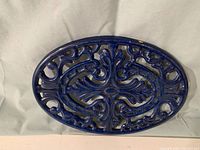Top view showing ornate enameled blue metal trivet with intricate scrollwork cutouts.