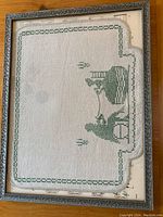 Framed needlework view showing entire piece, silvery wooden frame, and sheet music background