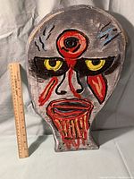 Front view of the painted wooden ghoul head with clear view of face markings and bullet hole.