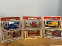 Six Lledo cast iron collectible vehicle models in original packaging, including blue Esso tanker truck, red fire wagon, yellow Coke truck, and three horse-drawn stagecoaches.