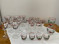 Wide view of all painted holiday glasses arranged on a cloth showing different styles including old fashioned, wine, tumblers, and shot glasses.