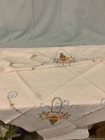 Full view of one linen table cover showing embroidered floral basket design and surrounding motifs