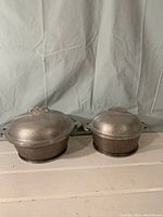Two matching hammered aluminum Dutch ovens with handles and lids, viewed frontally showing their shape and size difference.