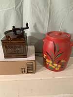Both cookie jars on shelf showing one resembling a coffee grinder and red floral painted jar