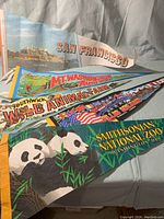 Five colorful vintage souvenir pennant banners spread out, showing names and images of attractions: Smithsonian National Zoo, Mt. Washington Auto Road, Southwick Wild Animal Farm, San Francisco Alcatraz, and Statue of Liberty.