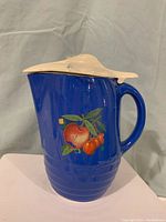 Cobalt blue pottery pitcher with apple design and lid, showing the front and handle.