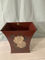 Front view of dark red wastebasket with hand-painted white chrysanthemums and green leaves on the front side.