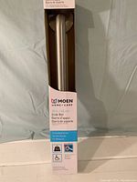 Full view of the boxed Moen 18-inch grab bar showing packaging and part of the product inside.