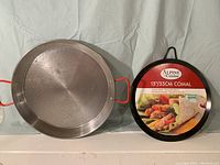 Photo showing a metallic 13-inch paella pan with red side handles next to a 13-inch Alpine Cuisine comal griddle with packaging label.