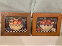Pair of framed country fruit prints by Diane Ulmer Pedersen on white background, showing entire lot with wood-tone frames