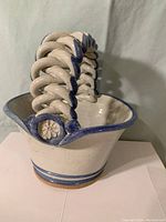 Side angle showing the woven rounded handle with blue glazing accents and smooth body of the flower basket.