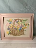 Full view of framed watercolor print of basket with colorful flowers and pink frame.