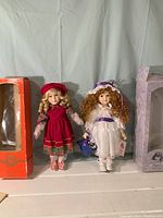 Two 10-inch collectable porcelain dolls displayed standing between their boxes, showing front view and overall condition.