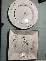 Top view of both plates showing the round plate with black dots and lines design and the square plate with black floral design on white background.